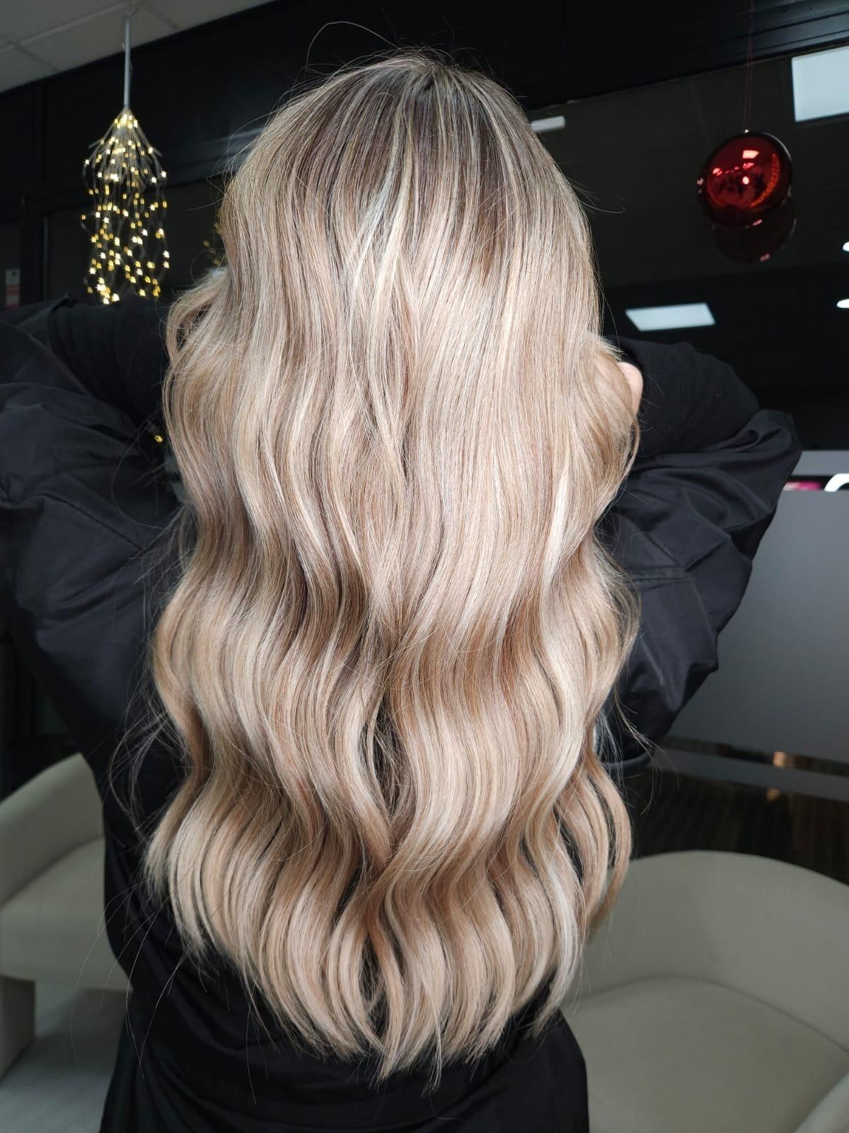 Mujer con cabello castaño largo y rizado, mirando hacia la derecha, vistiendo una blusa rosa claro, sobre un fondo azul.