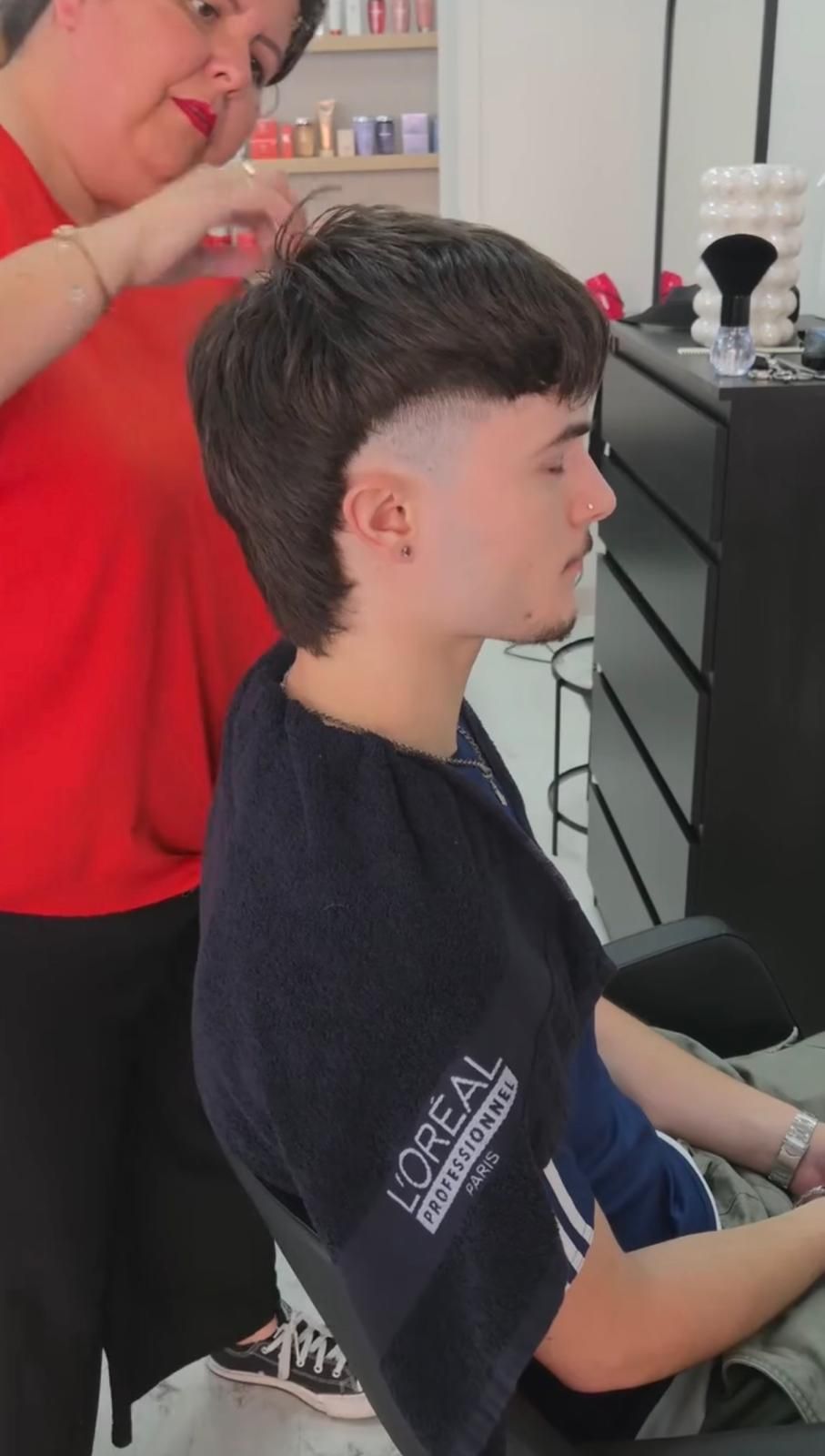 Hombre cortándose el pelo; barbero con tijeras y peine. Fondo oscuro.