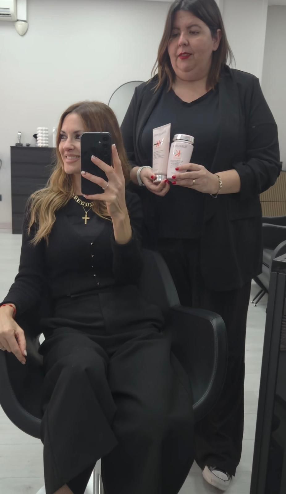 Mujer con cabello ondulado, desde raíces oscuras hasta puntas rubias, de pie en el interior.