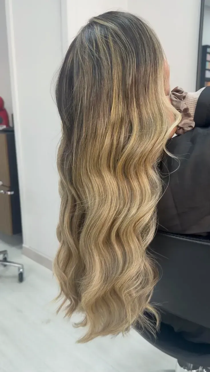 Cabello rubio ceniza ondulado con raíces más oscuras que caen en cascada.