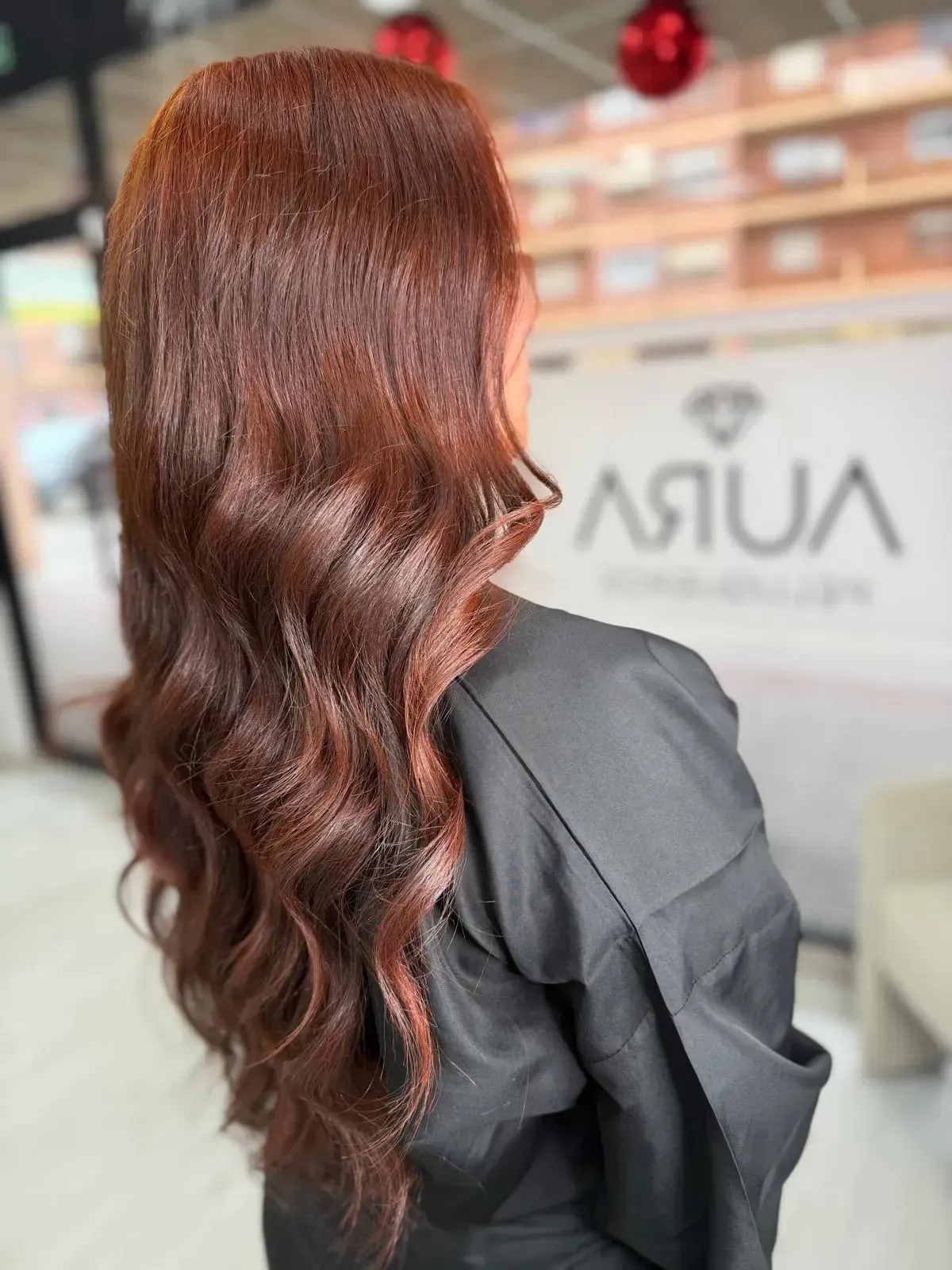 Una mujer con cabello rubio ondulado se apoya contra una pared de vidrio, mirando hacia la cámara.