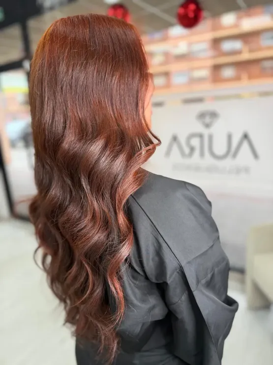 Una mujer con cabello rubio ondulado se apoya contra una pared de vidrio, mirando hacia la cámara.