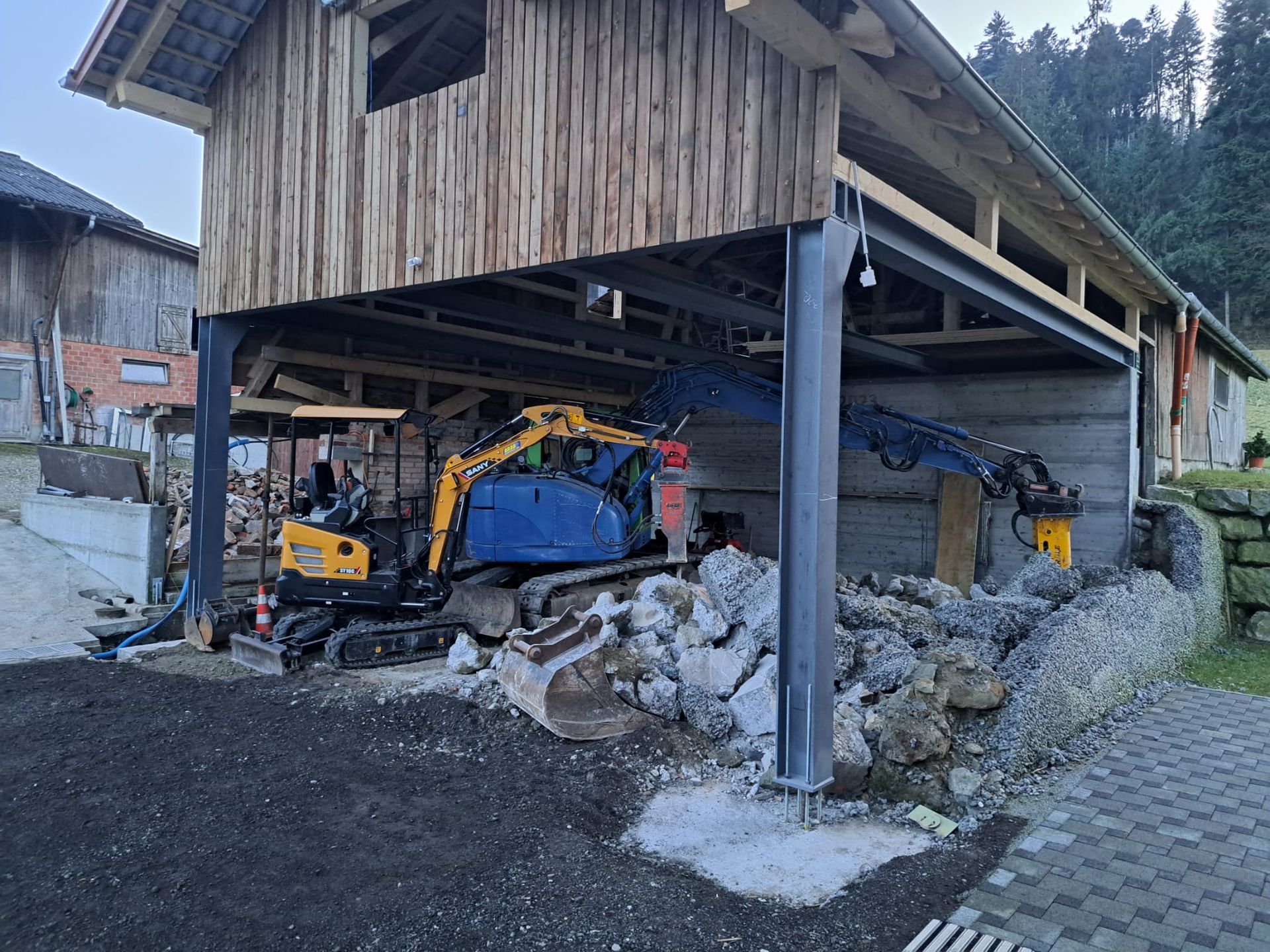 Ein gelber Hochleistungsbagger demontiert ein grosses, teilweise zerstörtes Gebäude auf einer Abrissbaustelle.