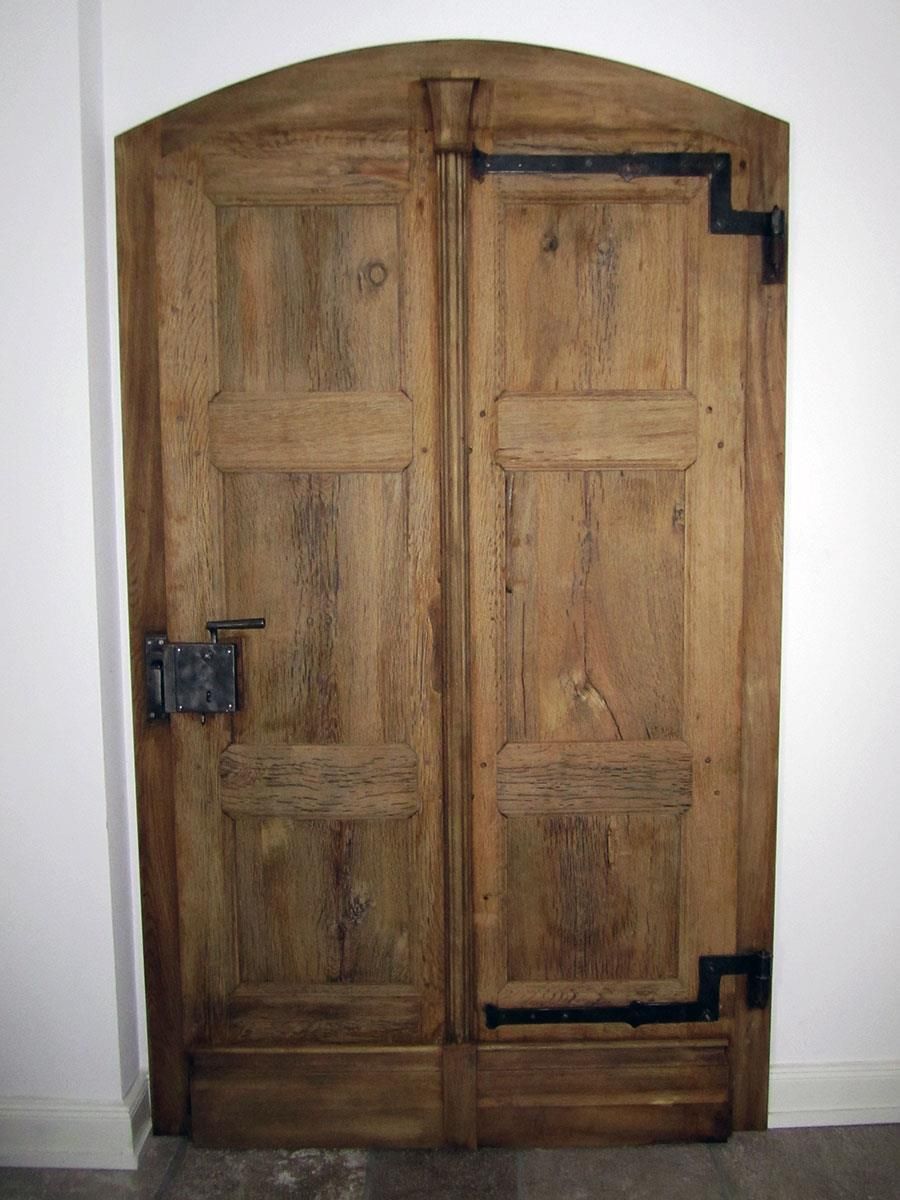 Eine Holztür mit einem Metallriegel steht vor einer weißen Wand