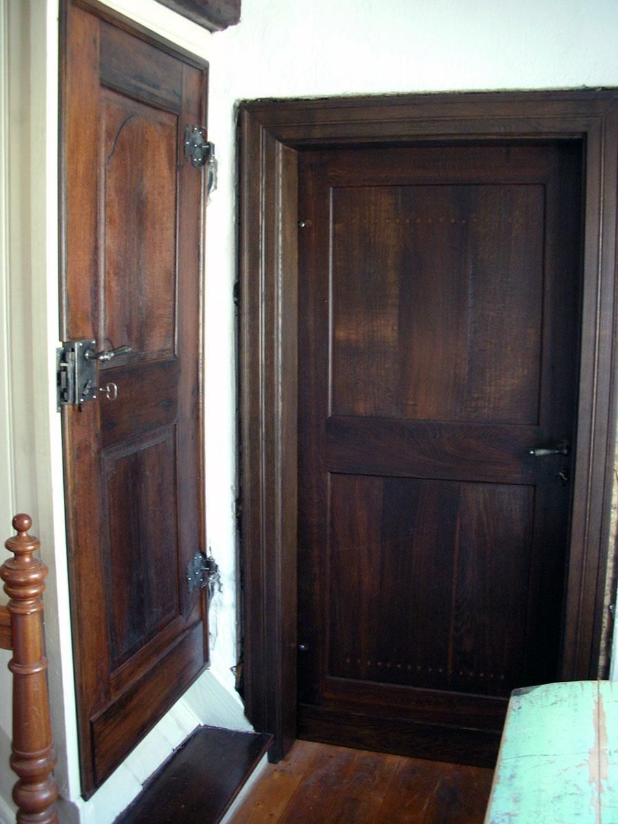 In einem Zimmer neben einem Bett steht eine Holztür offen