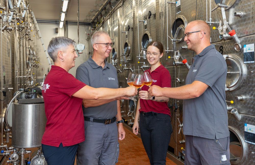 Eine Gruppe Menschen stößt in einem Weingut mit Weingläsern an.
