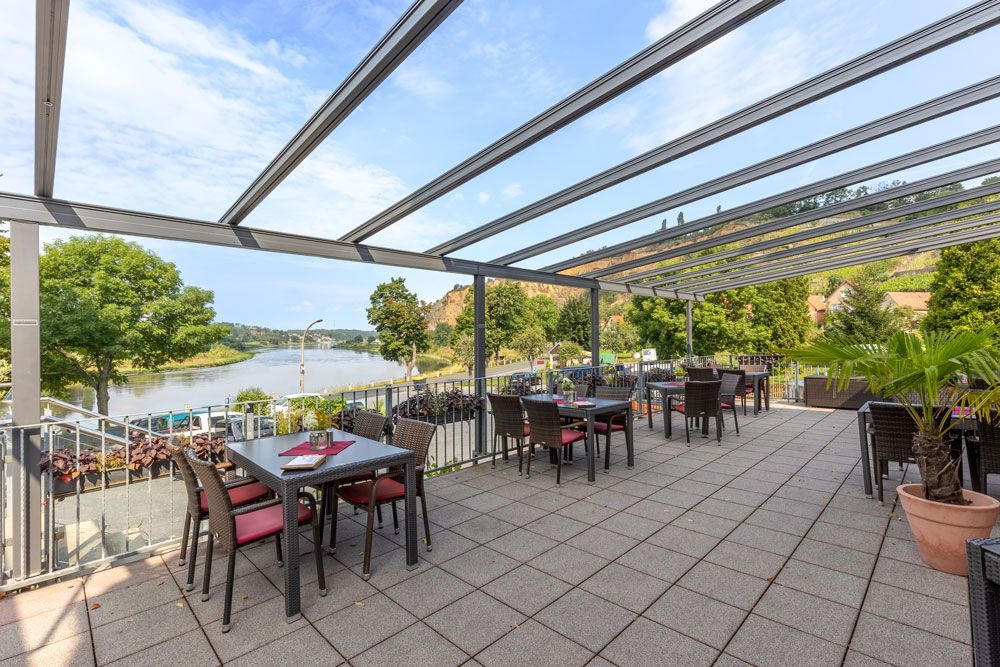 Eine Terrasse mit Tischen und Stühlen mit Blick auf einen Fluss.