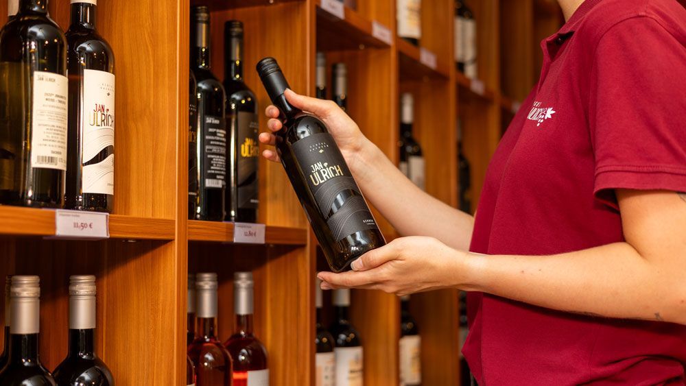 Eine Frau hält eine Flasche Wein vor einem Regal voller Weinflaschen.