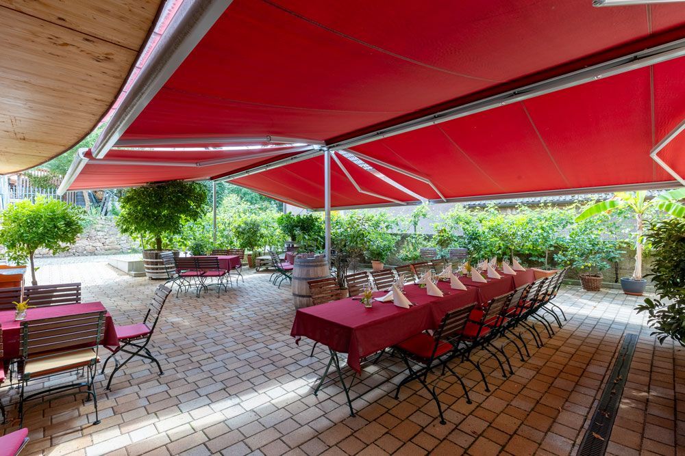 Eine Terrasse mit Tischen und Stühlen unter roten Markisen.