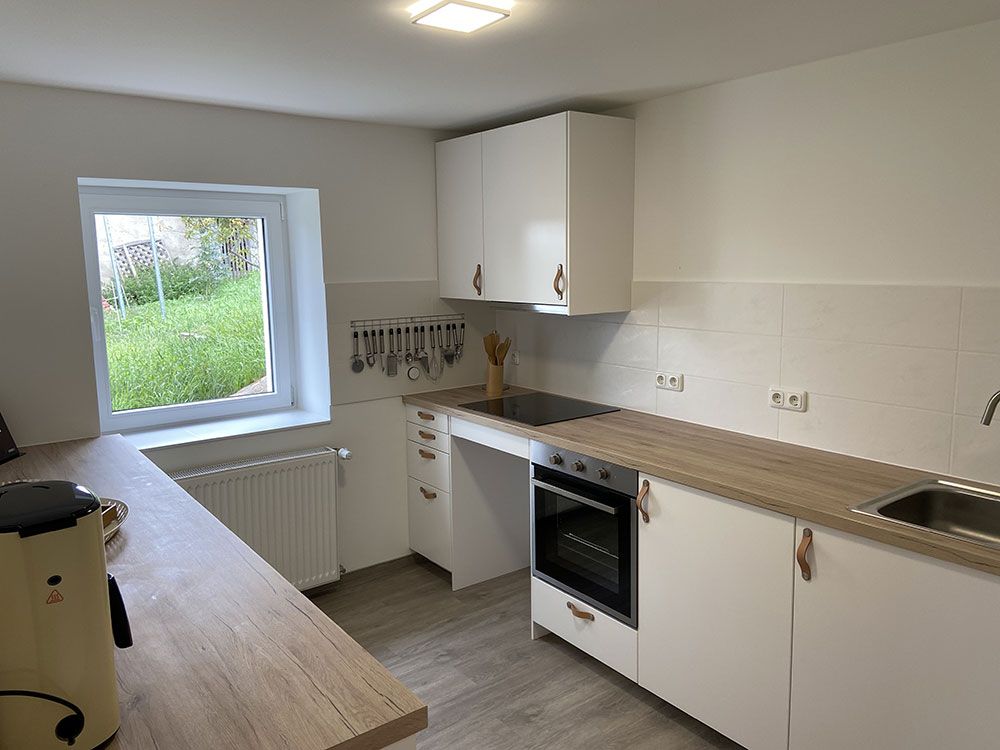 Eine Küche mit weißen Schränken, einem Herd, einer Spüle und einem Fenster.