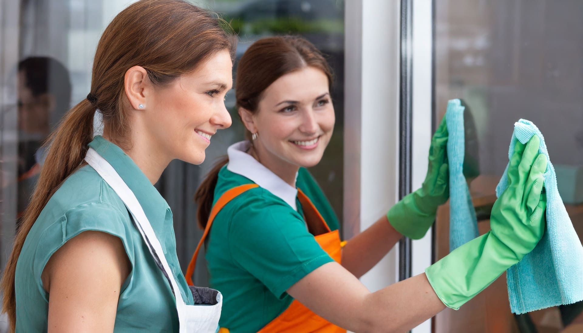 Zwei Frauen in grünen Handschuhen reinigen ein Fenster | MMJ Glas- und Gebäudereinigung