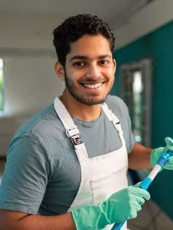 Ein Mann in einer Schürze und Handschuhen hält einen Besen und lächelt | MMJ Glas- und Gebäudereinigung