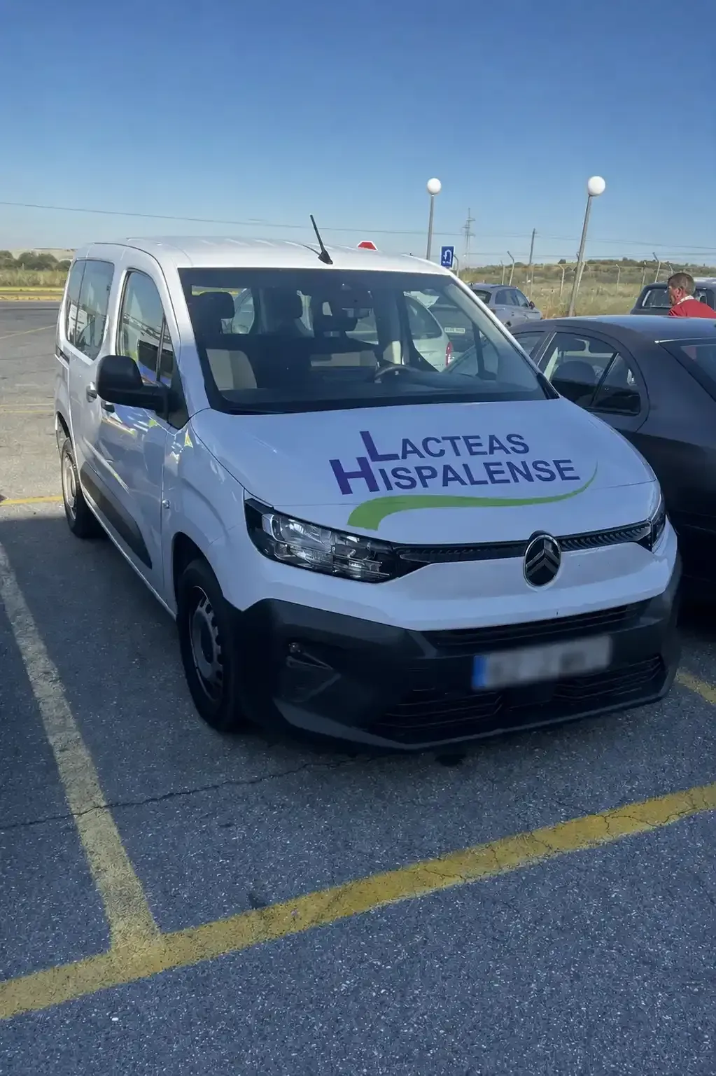 Una furgoneta de reparto blanca con el logotipo de “Lacteas Hispalegense” aparcada en un estacionamiento bajo un cielo azul.