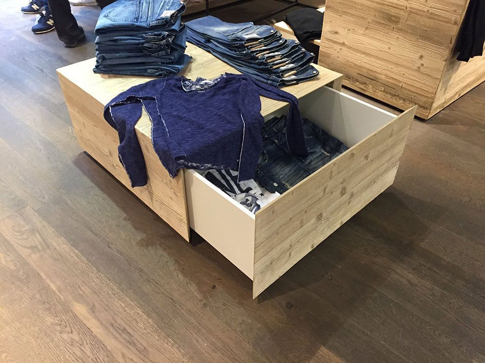 Ein Holztisch mit einer Schublade voller Kleidung in einem Geschäft.