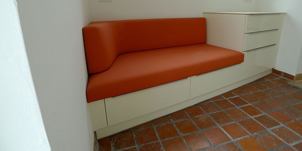 In einer Zimmerecke steht ein Sofa mit orangefarbenen Kissen.