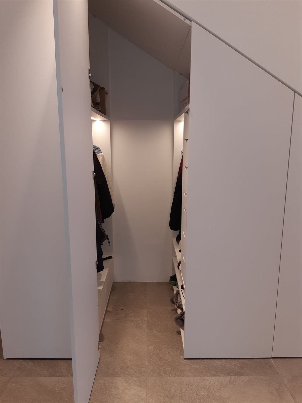 Ein begehbarer Kleiderschrank unter einer Treppe mit an der Wand hängender Kleidung.