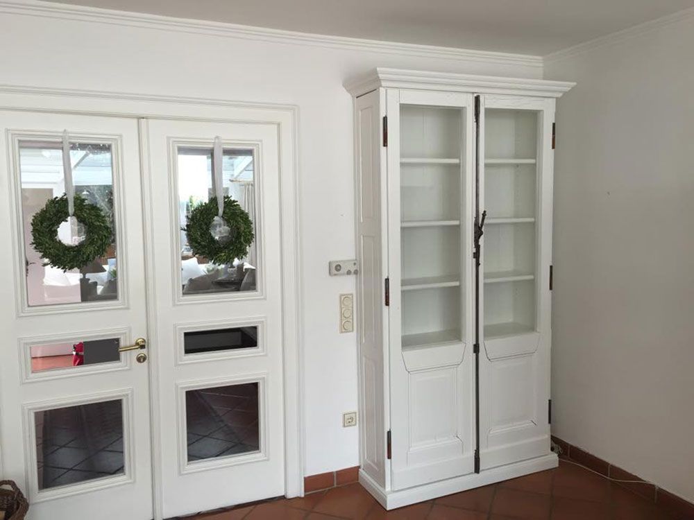 In einem Raum steht neben zwei Türen ein weißer Schrank mit Glastüren.
