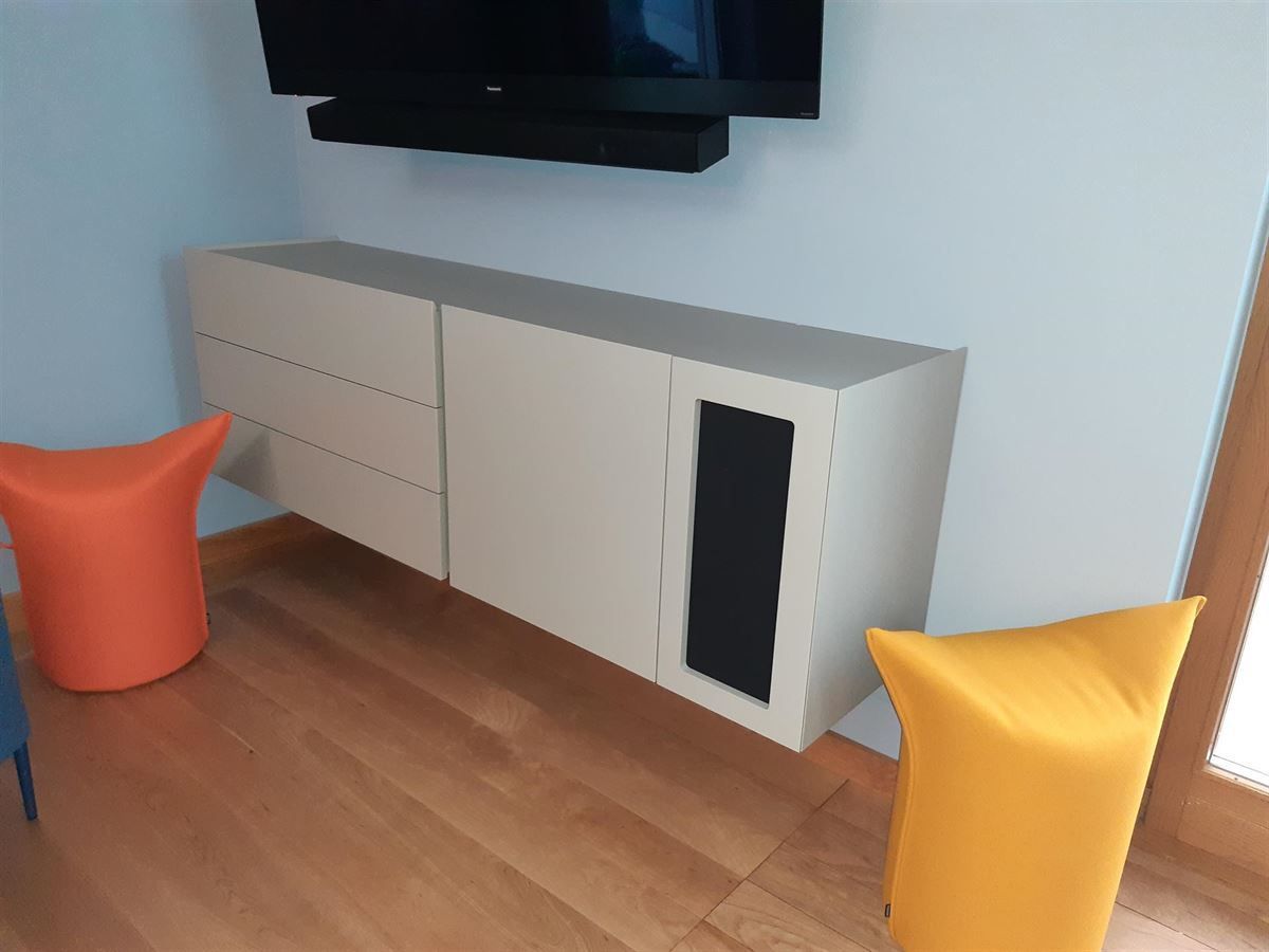 Ein Wohnzimmer mit einem Fernseher an der Wand und zwei Ottomanen