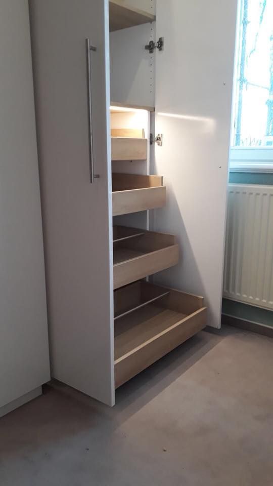 Ein weißer Schrank mit Holzregalen und Schubladen in einem Raum neben einem Fenster.