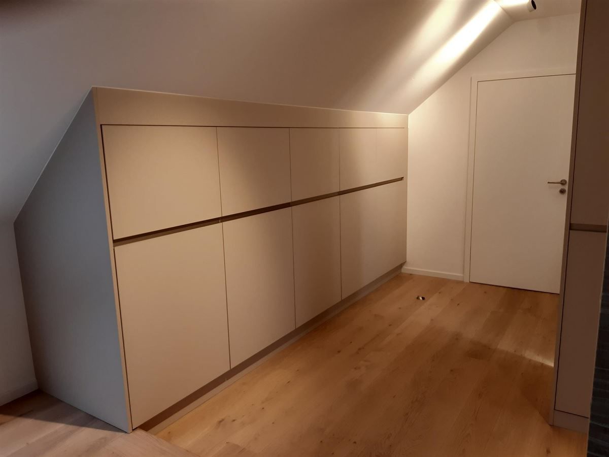 Ein Raum mit schräger Decke und weißen Schränken