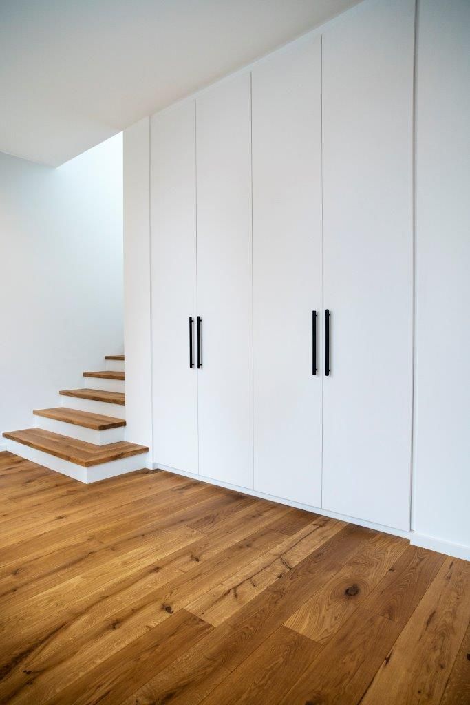 Ein leerer Raum mit Holzböden und weißen Schränken und Treppen.