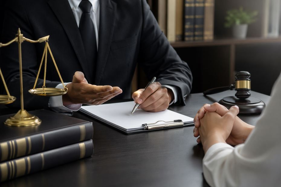 Un abogado consulta con un cliente en un escritorio, con una balanza de la justicia y documentos legales cerca.