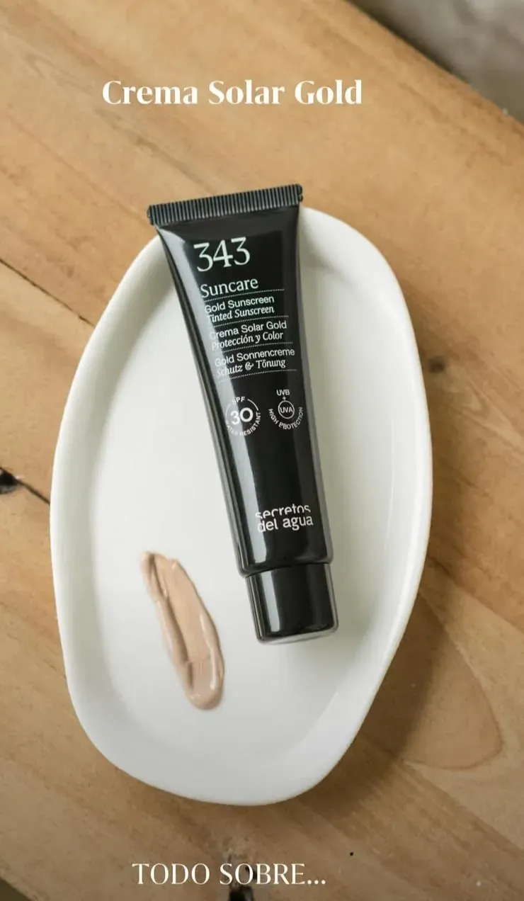 Tubo de protector solar con FPS 50+ sobre un plato ovalado blanco en una mesa de madera, con una pequeña muestra de crema.