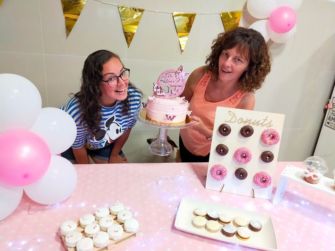 Dos mujeres están sentadas en una mesa con un pastel y donas.