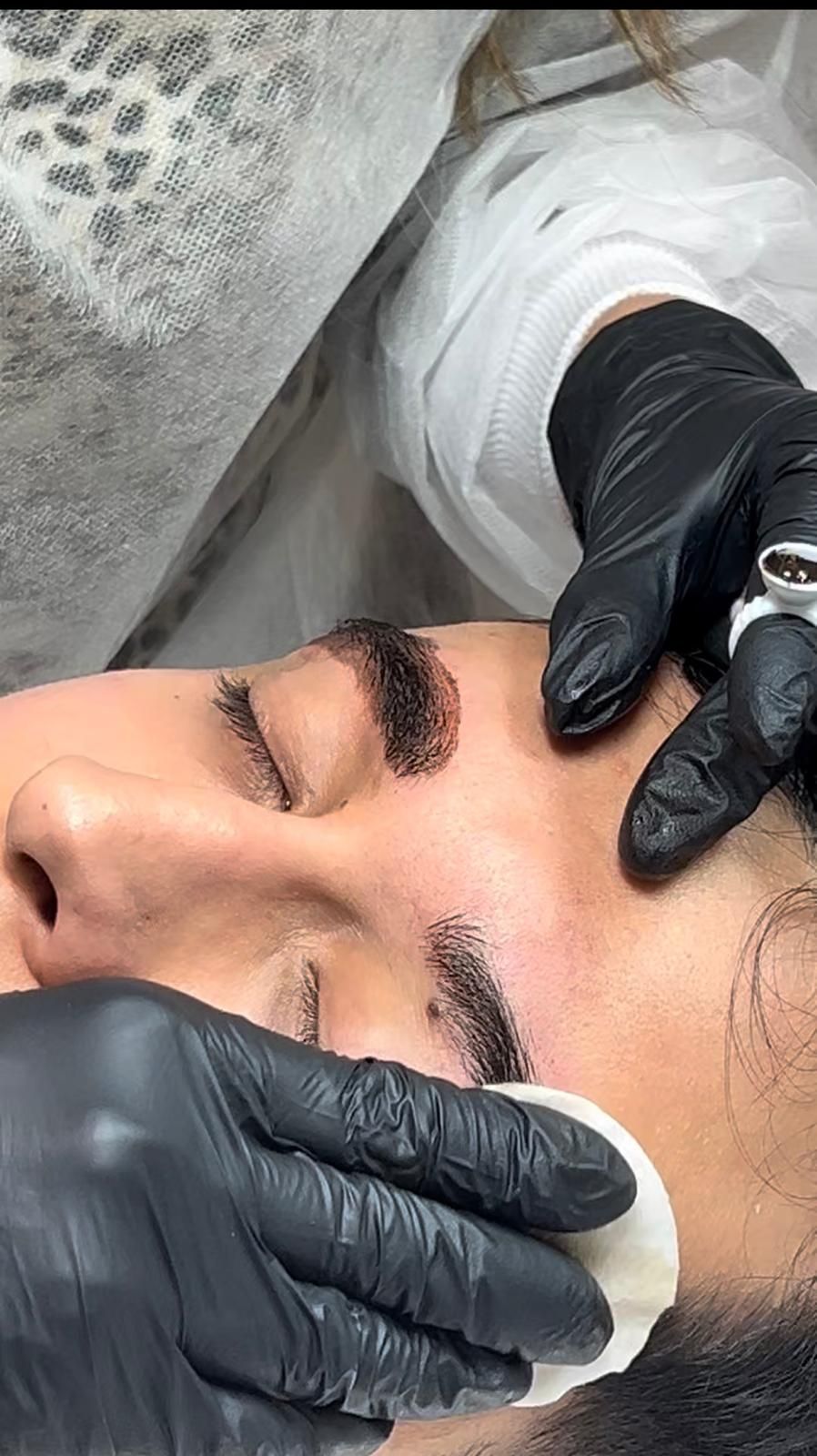 Manos enguantadas limpiando el rostro de un cliente con discos de algodón durante un tratamiento facial.