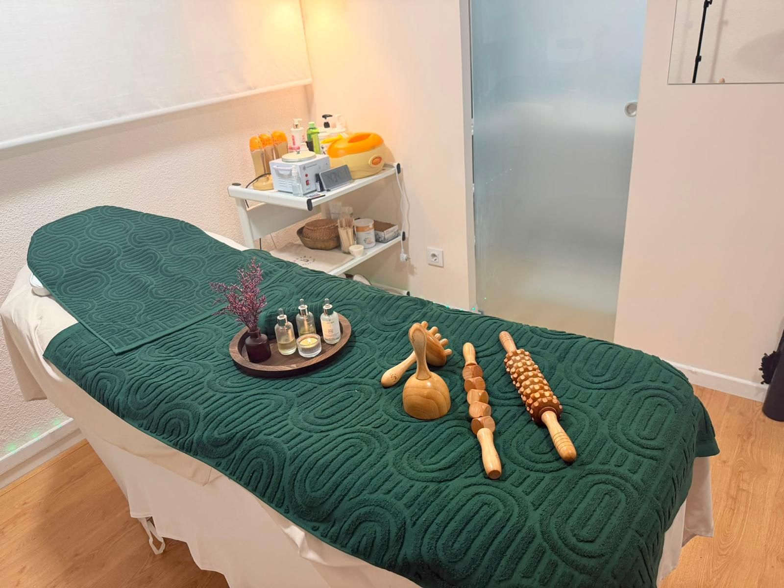 Sala de tratamientos de spa con camilla de masaje, toalla verde oscuro y herramientas de masaje en una bandeja.