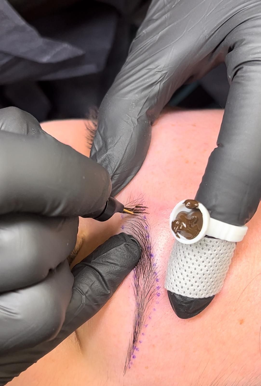 Unas manos enguantadas realizan un tatuaje sobre piel rosada junto a una venda adhesiva blanca.
