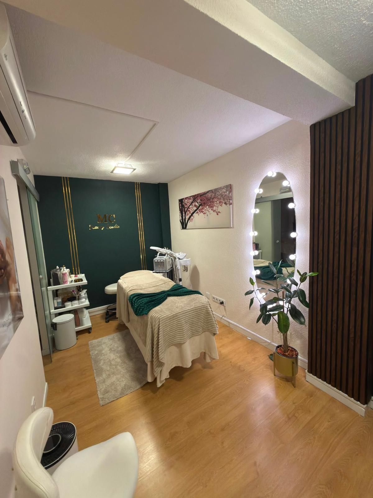 Sala de masajes con camilla de tratamiento, pared decorativa color turquesa, tocador con espejo y suelo de madera cálida.