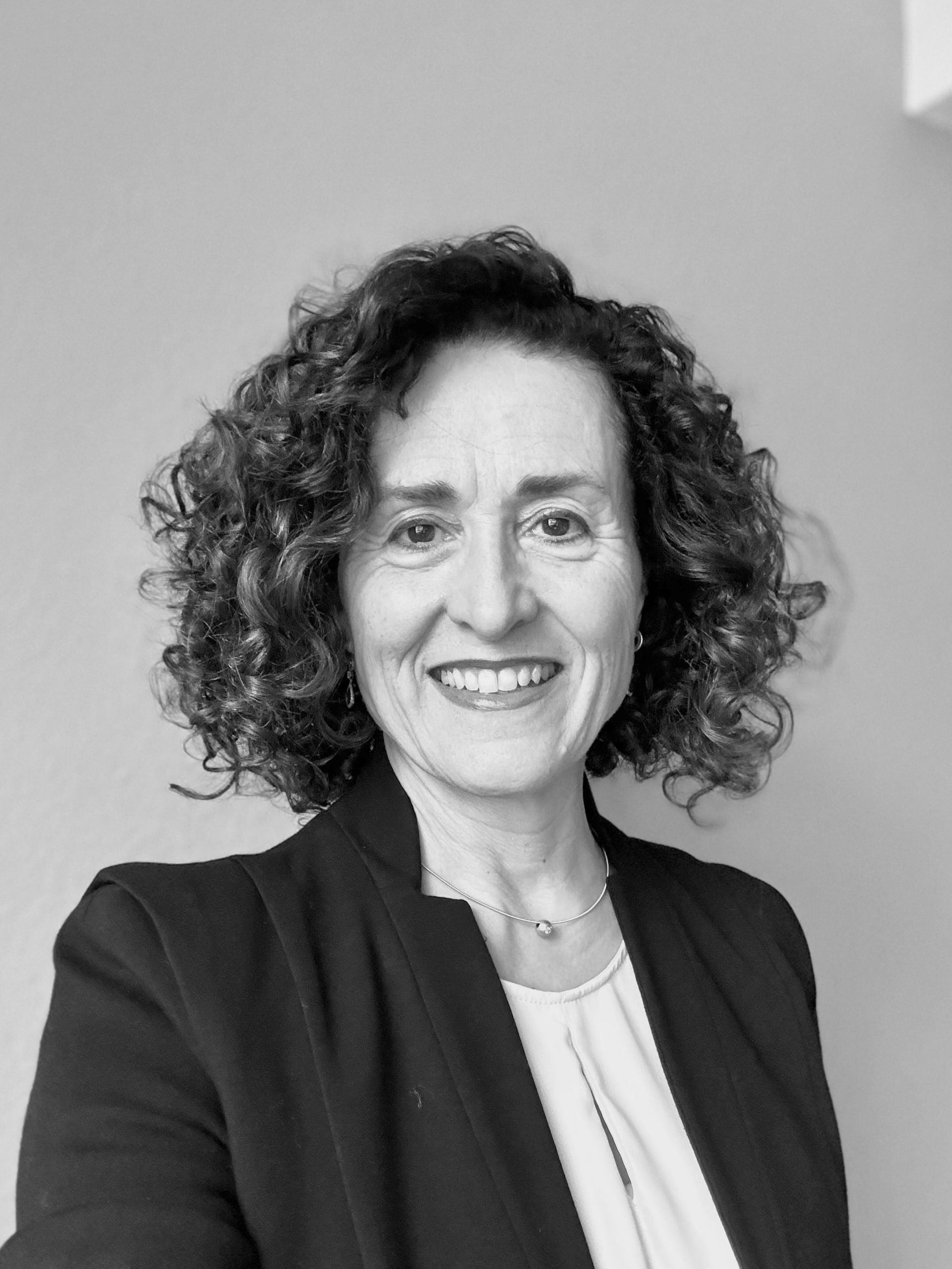 Frau mit lockigem Haar lächelt, sie trägt einen Blazer.