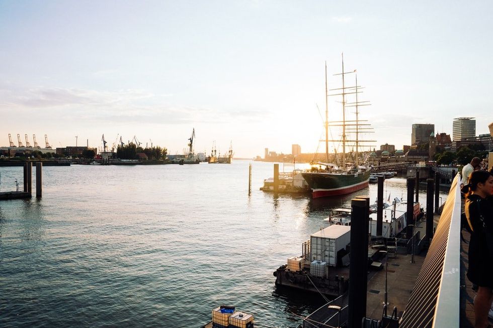 Hafen bei Sonnenuntergang mit großem Segelschiff, Docks und Stadtkulisse.