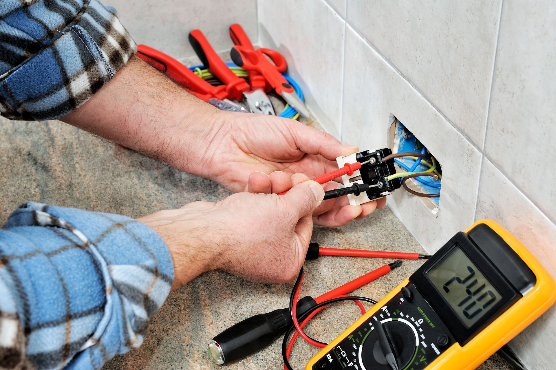 Électricien utilisant un multimètre sur les fils de prise, avec des outils à proximité.