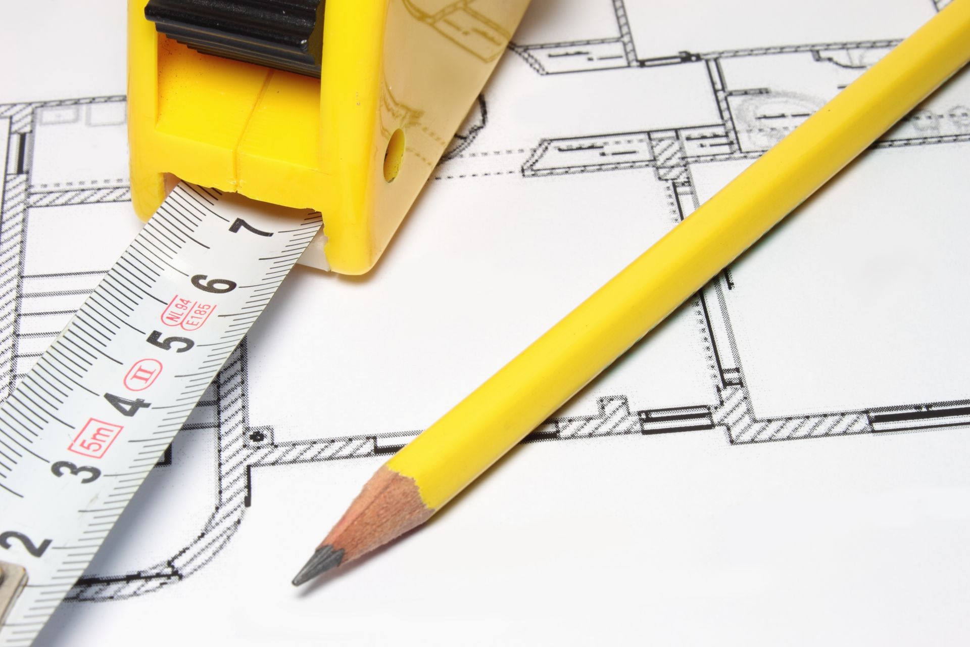 Ruban à mesurer jaune et crayon sur un plan, suggérant des travaux de construction ou de conception.