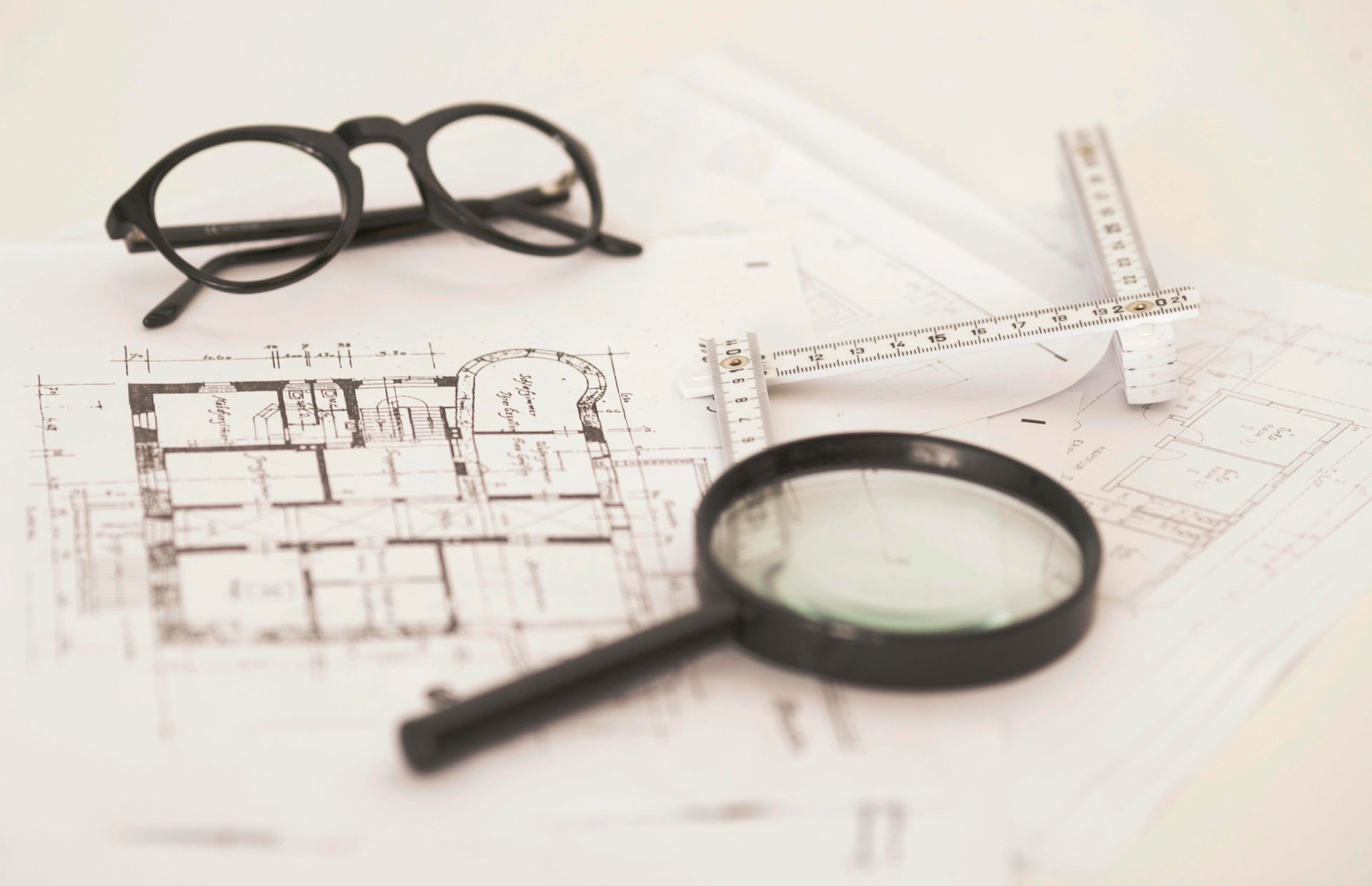 Lunettes à monture noire, loupe et règle sur des plans architecturaux.