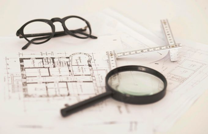Lunettes à monture noire, loupe et règle sur des plans architecturaux.