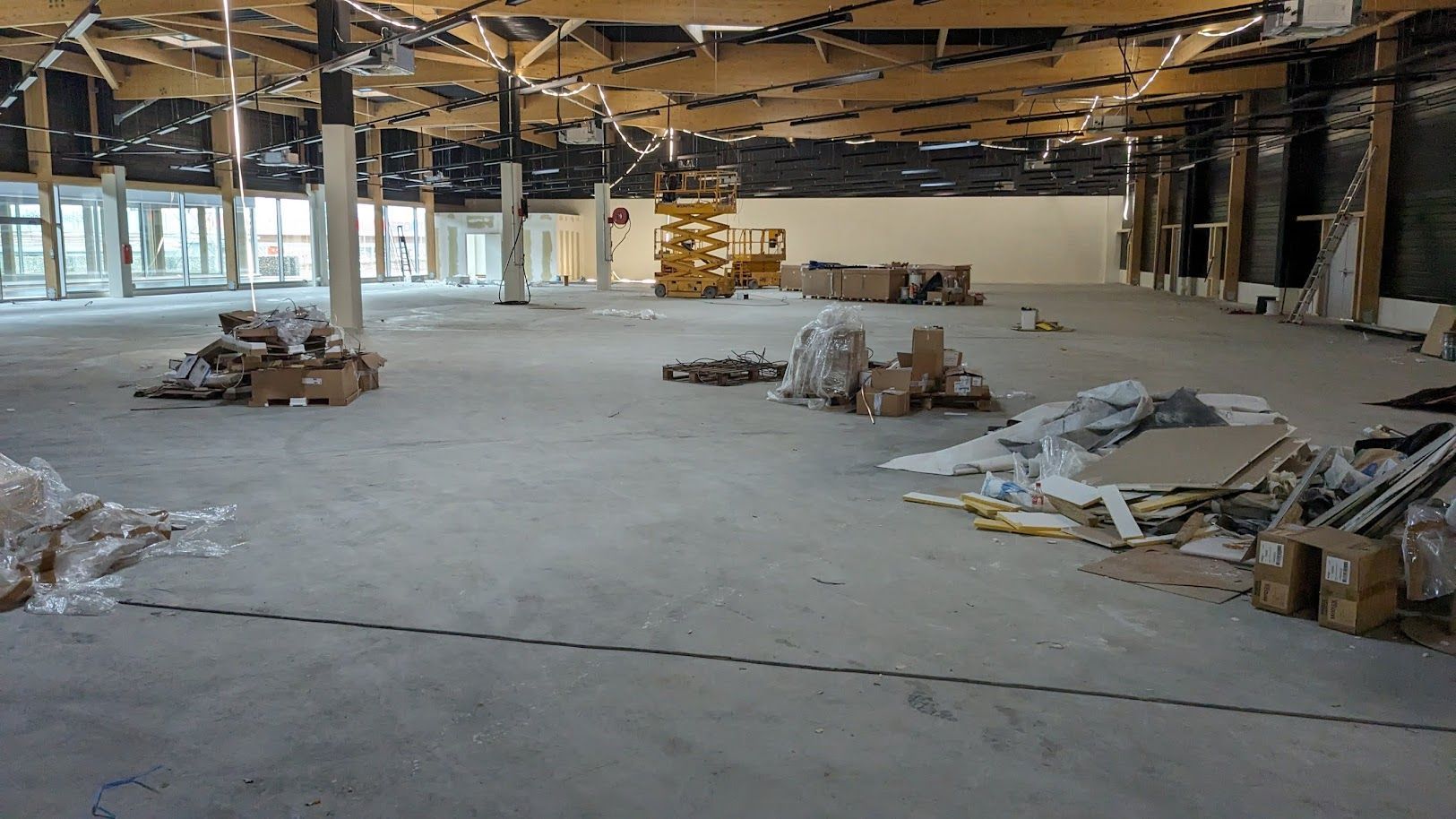 Intérieur de bureau vide et inachevé, avec plafond apparent, matériaux de construction éparpillés et sol en béton.
