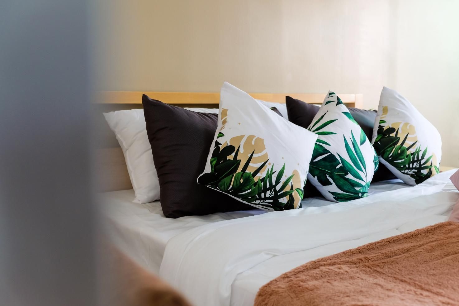 Cama con sábanas blancas, almohadas marrones y florales y una manta color melocotón.