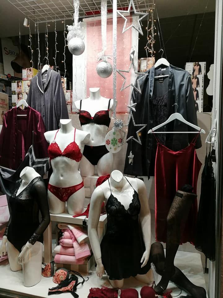 Escaparate de una tienda de lencería: maniquíes con lencería negra y roja variada. Decoración navideña e iluminación tenue.