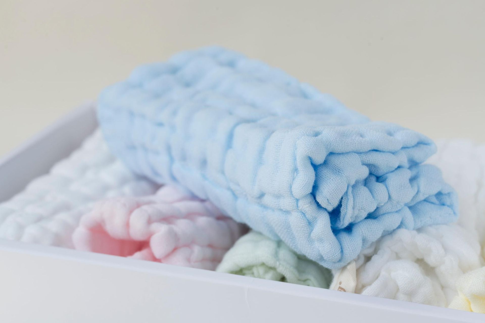 Toallitas de colores pastel apiladas en una bandeja blanca. Una toallita azul está arriba, y una blanca, rosa y verde abajo.