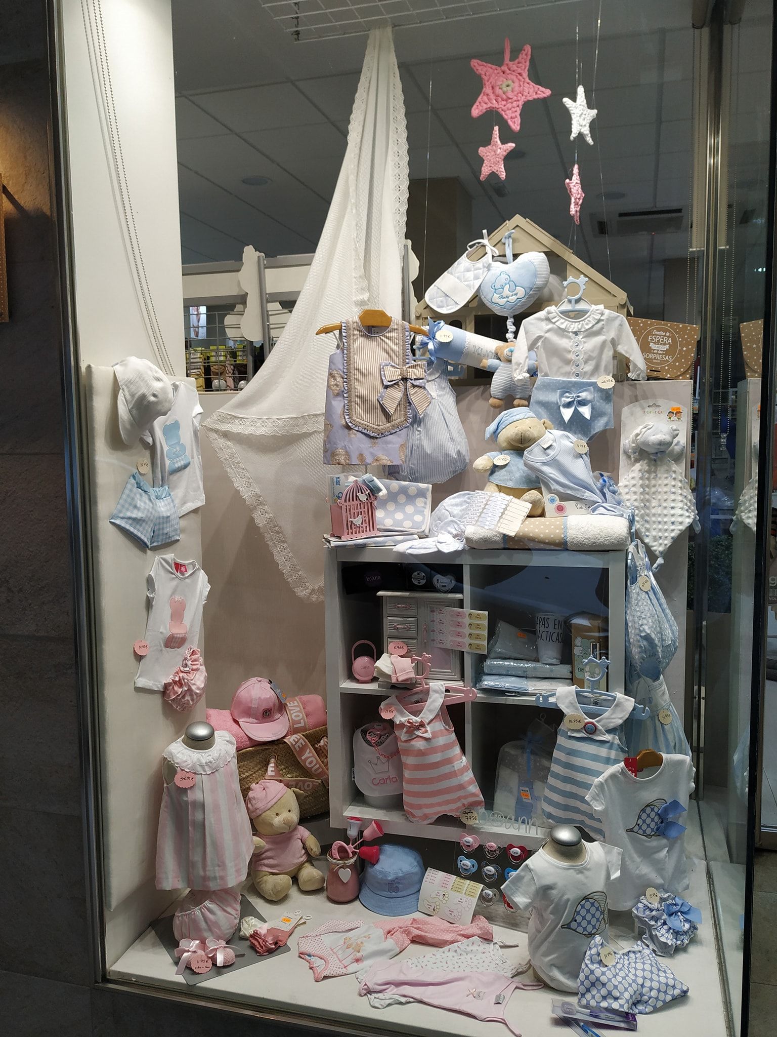 Escaparate de tienda con ropa de bebé en tonos pastel rosa y azul.