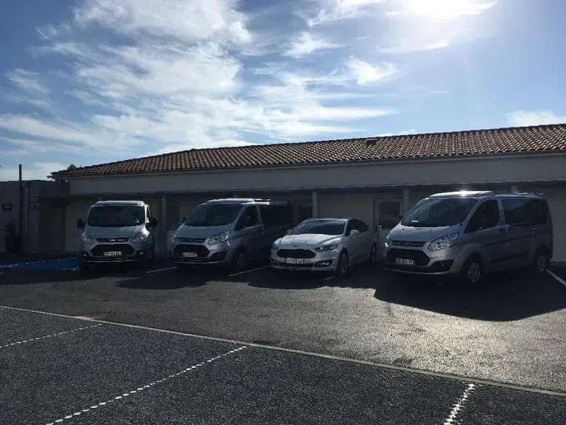 Quatre véhicules argentés stationnés devant un bâtiment sous un ciel partiellement nuageux.