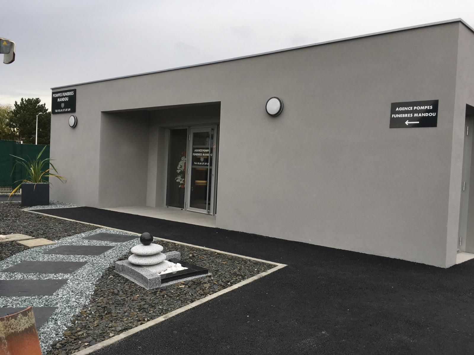 Entrée d'un bâtiment gris avec des touches de noir et un aménagement paysager.