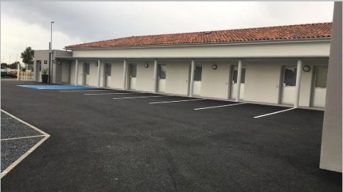 Une pièce avec une table de massage, deux chaises et un lampadaire. Les murs sont blancs et le sol foncé.