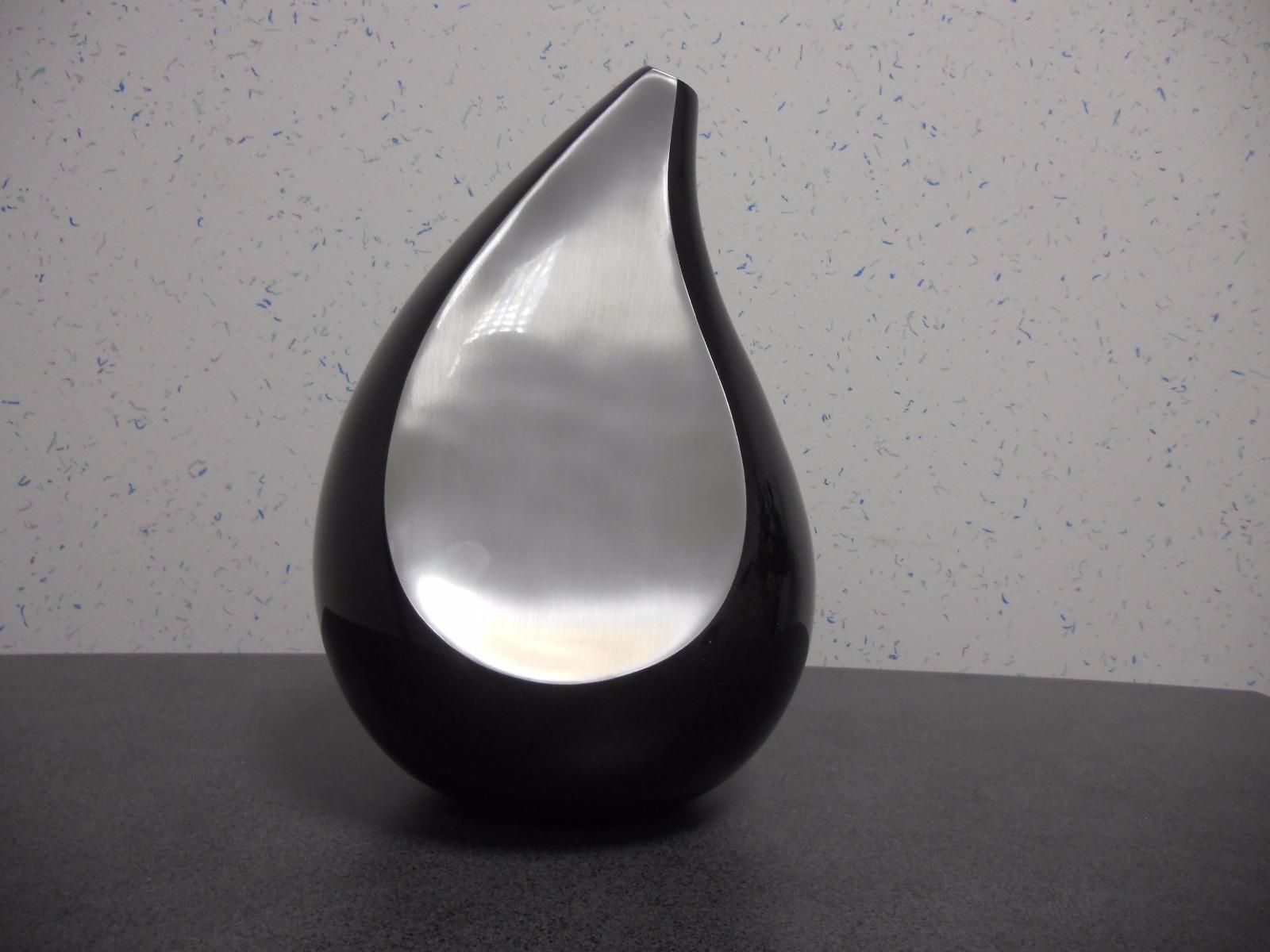 Sculpture noire en forme de larme à l'intérieur argenté, posée sur une surface sombre.