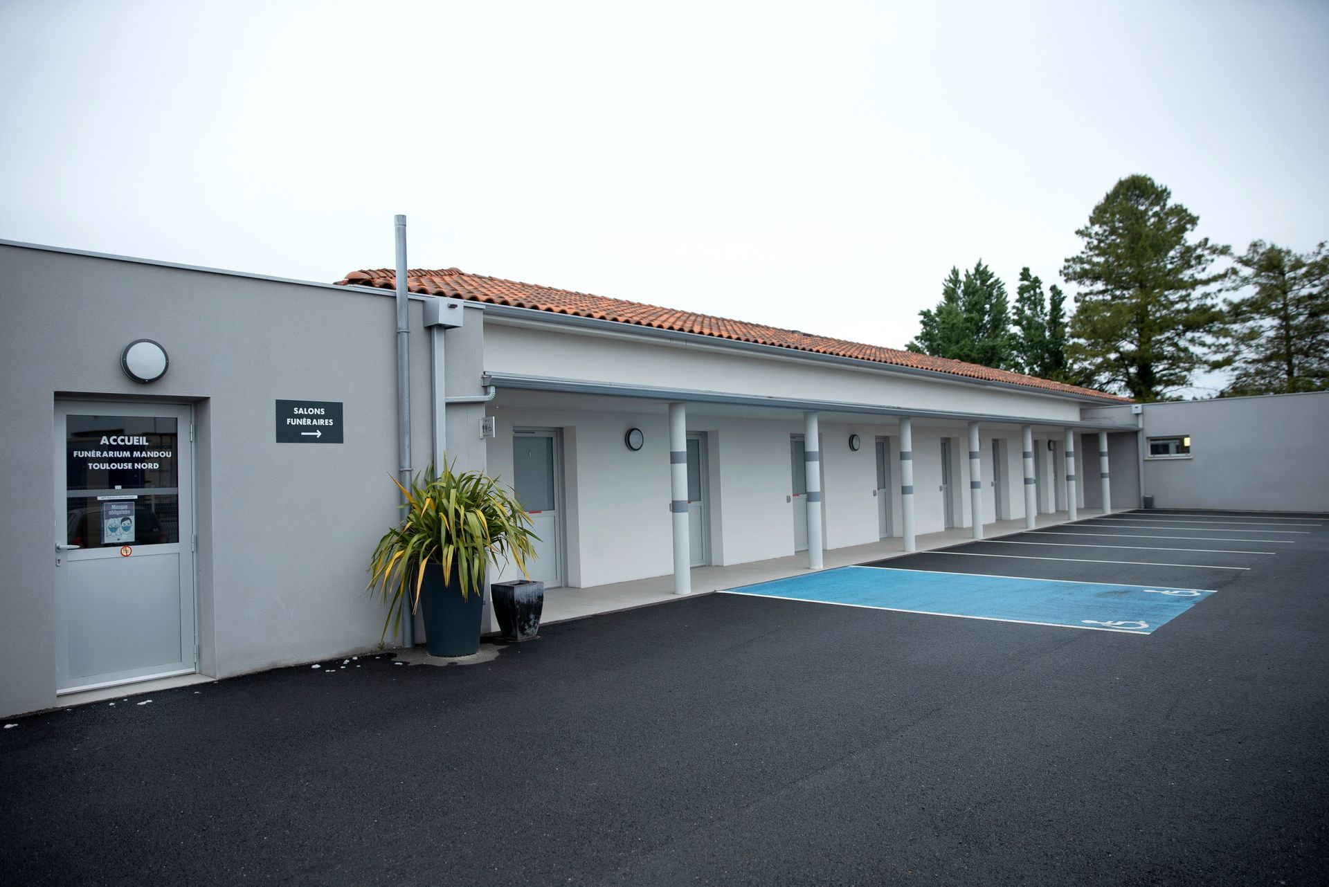 Salle d'attente avec carrelage foncé, meubles en osier et petite télévision au mur.
