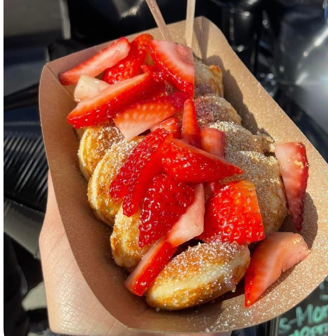 Personne tenant un dessert dans un bateau en papier : mini-crêpes aux fraises, guimauves et vermicelles.