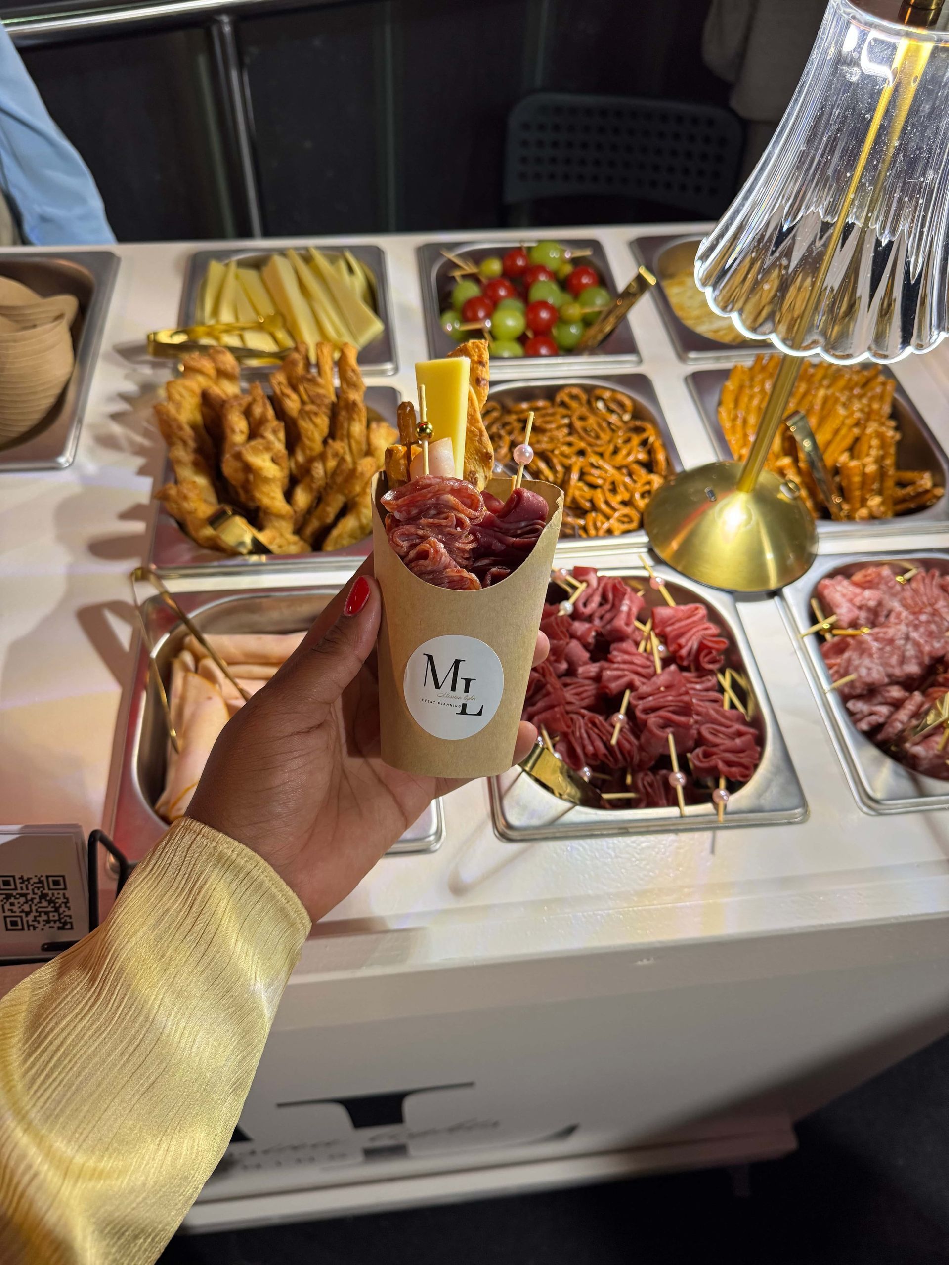 Un bar à desserts avec garnitures, dans un restaurant à l'éclairage tamisé et coloré. On aperçoit des tables nappées de blanc.